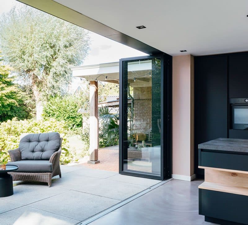Geopende antraciet glazen pui op de hoek van een keuken, met een loungestoel op het terras