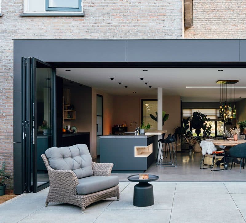 Antraciet glazen schuifpui geopend tussen terras en woonkeuken in een bakstenen woning