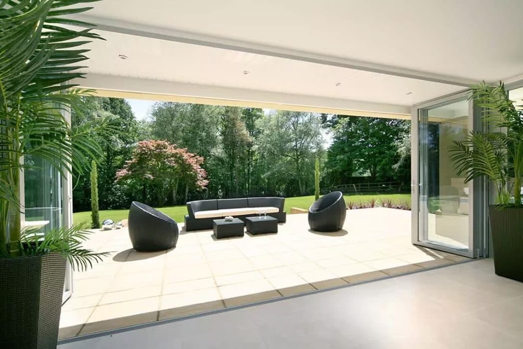 Geopende vouwwand van een glazen aanbouw met zicht op een tuin met loungeset