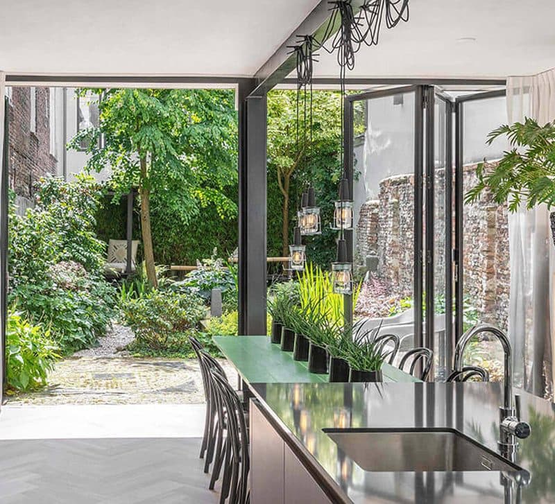 Keuken met kookeiland en een geopende glazen pui naar een groene binnenplaats