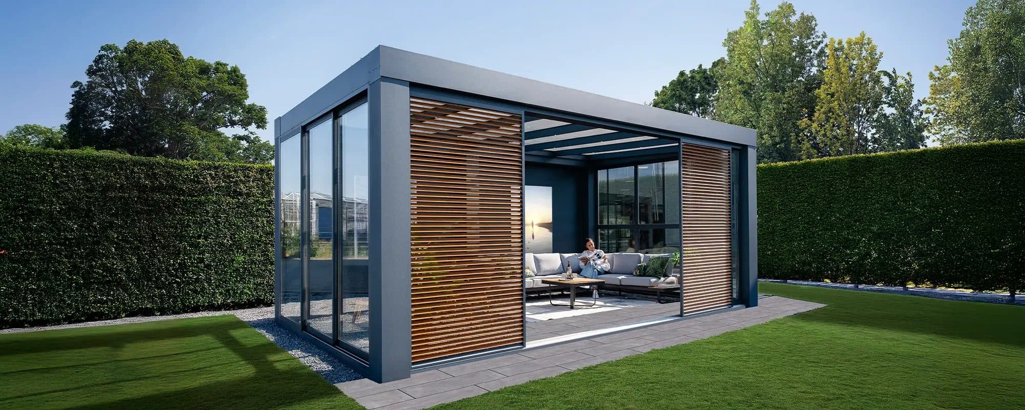 Vrijstaande antraciet overkapping met houtkleurige lamellen schuifwanden en glazen wanden in een tuin met hagen