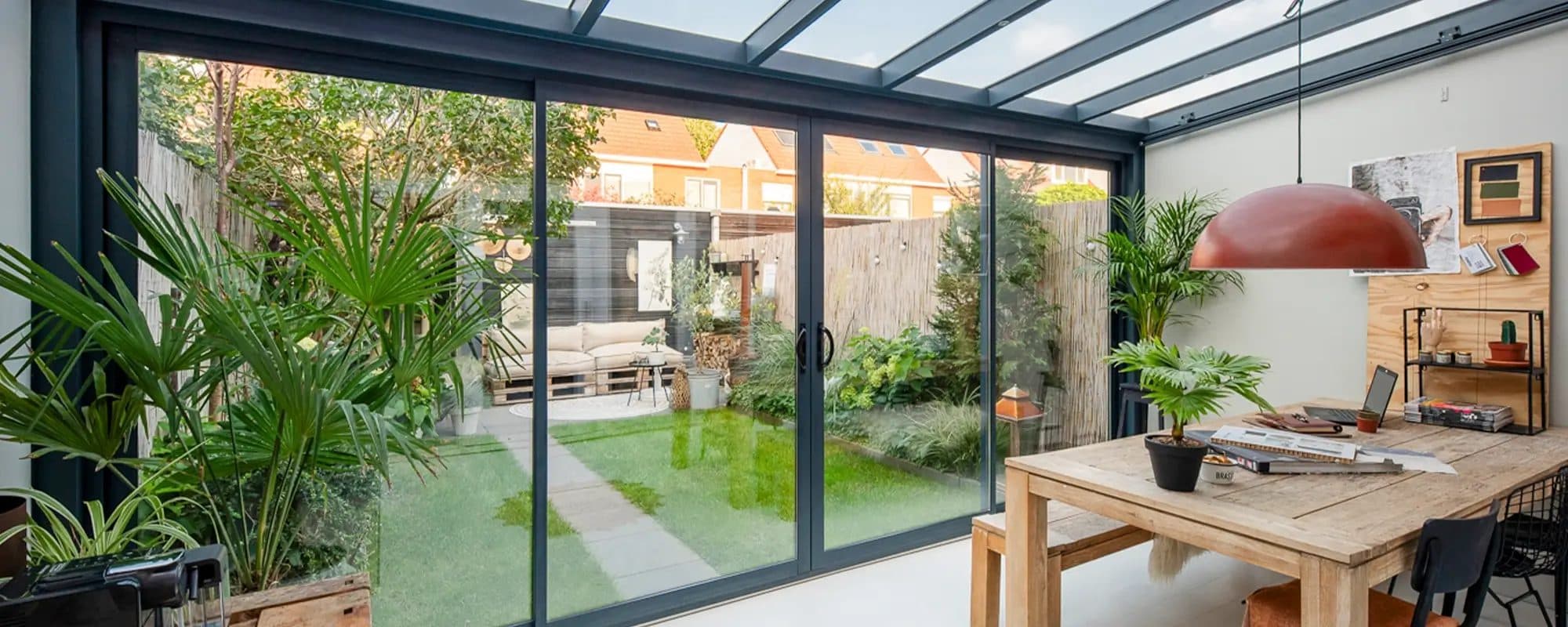 Werktafel en planten in een tuinkamer met antraciet aluminium schuifpui naar een stadstuin