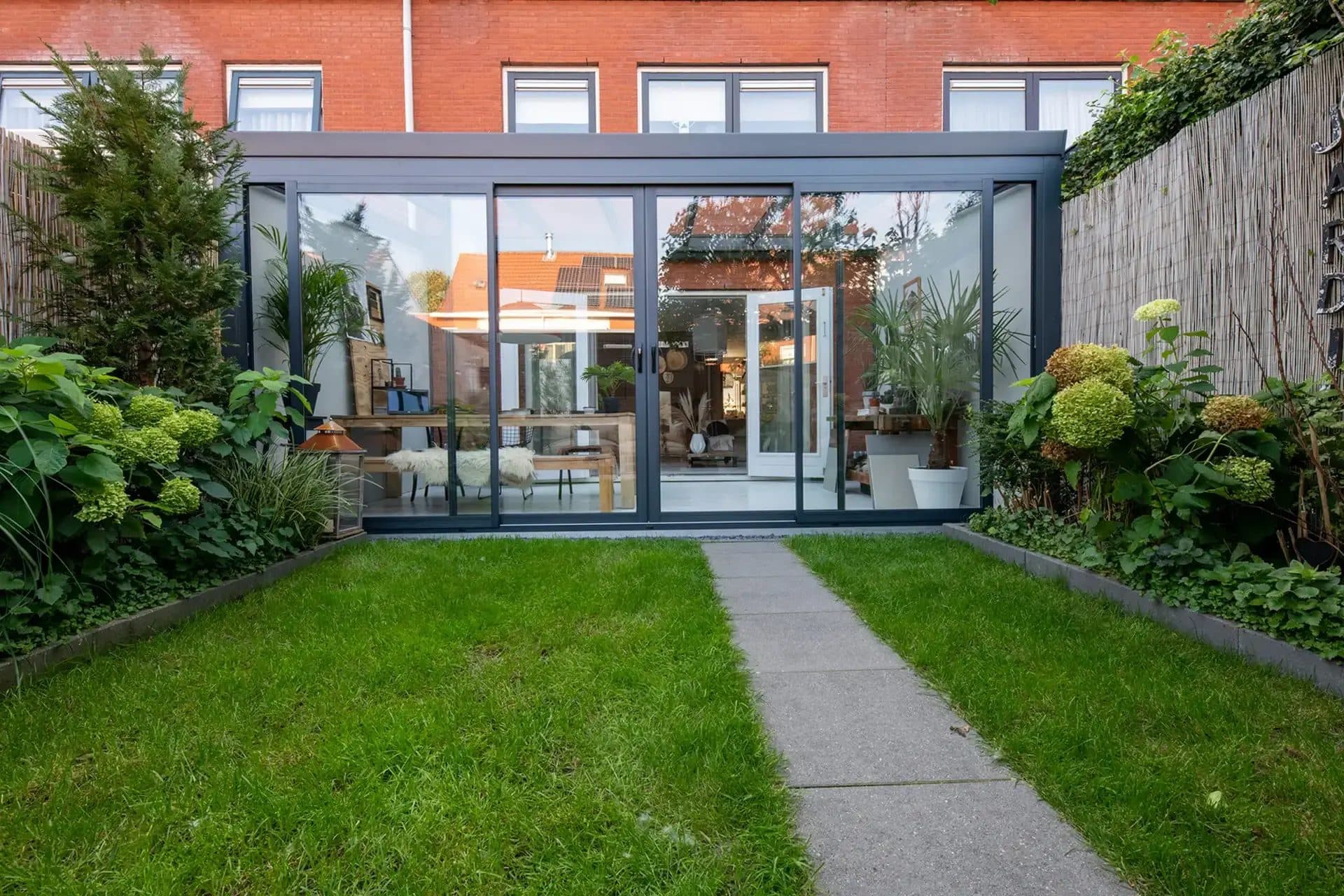 Tuinkamer met antraciet aluminium schuifpui aan het eind van een smalle stadstuin met gazon