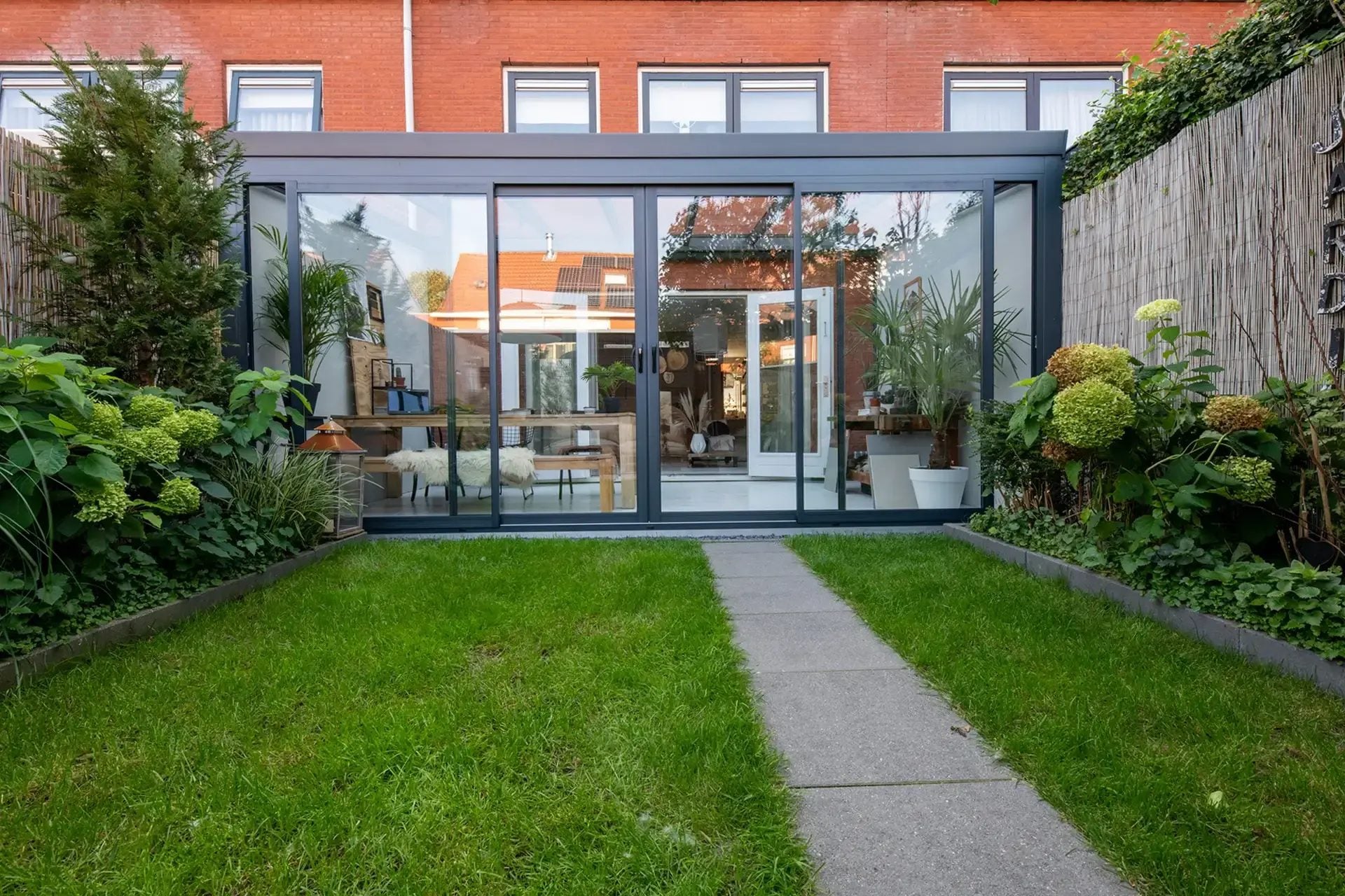 Tuinkamer met antraciet aluminium schuifpui aan het eind van een smalle stadstuin met gazon