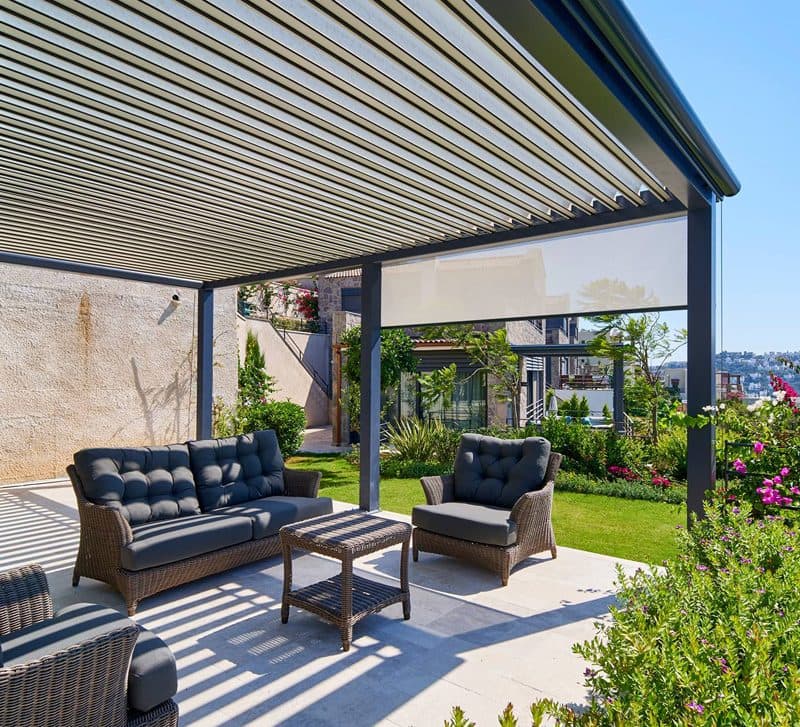 Antraciet lamellendak met een screen aan de zijkant boven een loungeset in een tuin