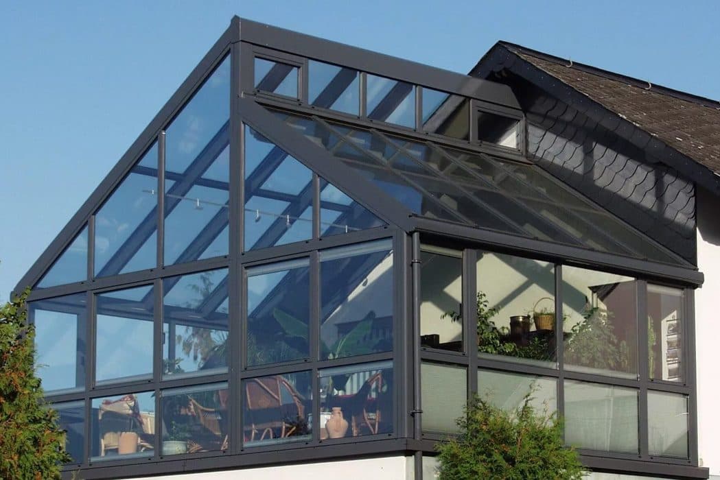Antraciet serre met glazen zadeldak tegen een woning, van onderaf gezien