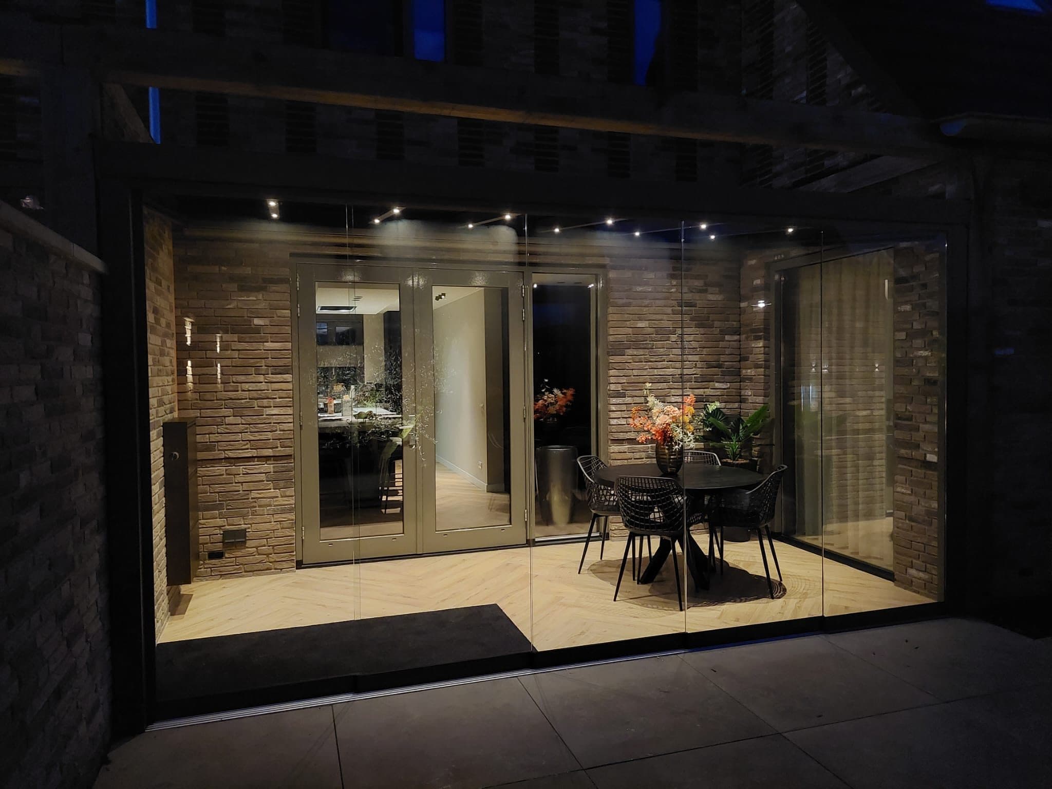 Veranda met glazen wanden 's avonds, met brandende spots in het dak boven een ronde eettafel