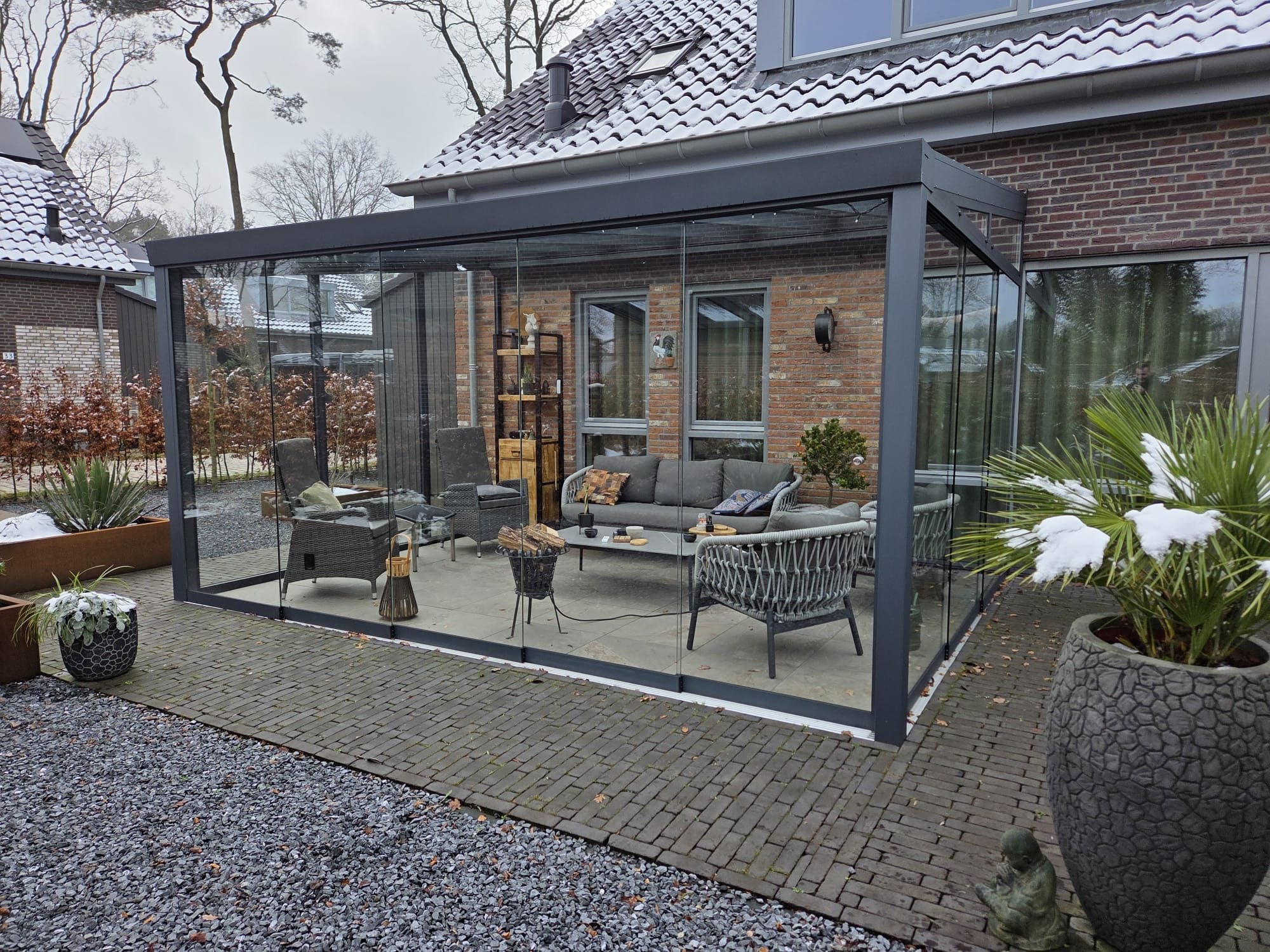 Antraciet veranda met rondom glazen schuifwanden en een loungeset, met sneeuw in de plantenbakken ervoor