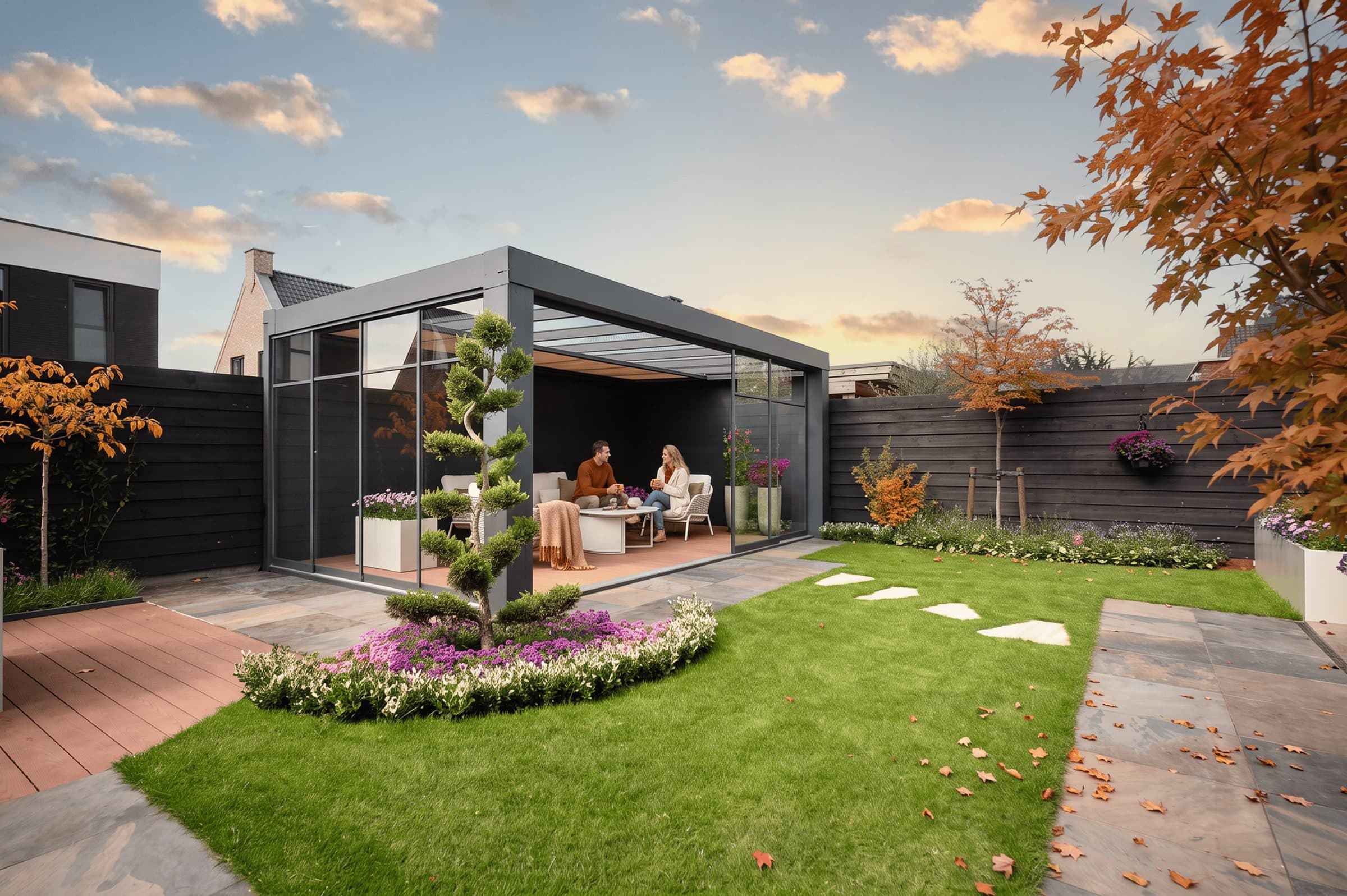 Twee mensen op de bank in een antraciet Cube met glazen wanden, in een tuin met herfstkleuren en een gesnoeid boompje