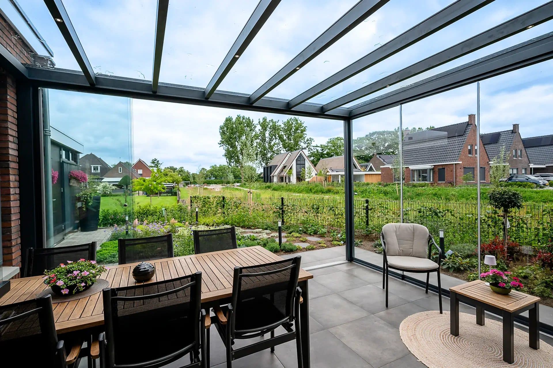 Eettafel onder een antraciet veranda met glasdak, met uitzicht op een tuin en weiland