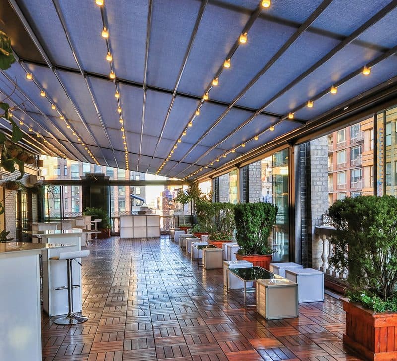 Overdekte lounge onder een vouwdak met lichtsnoeren en plantenbakken