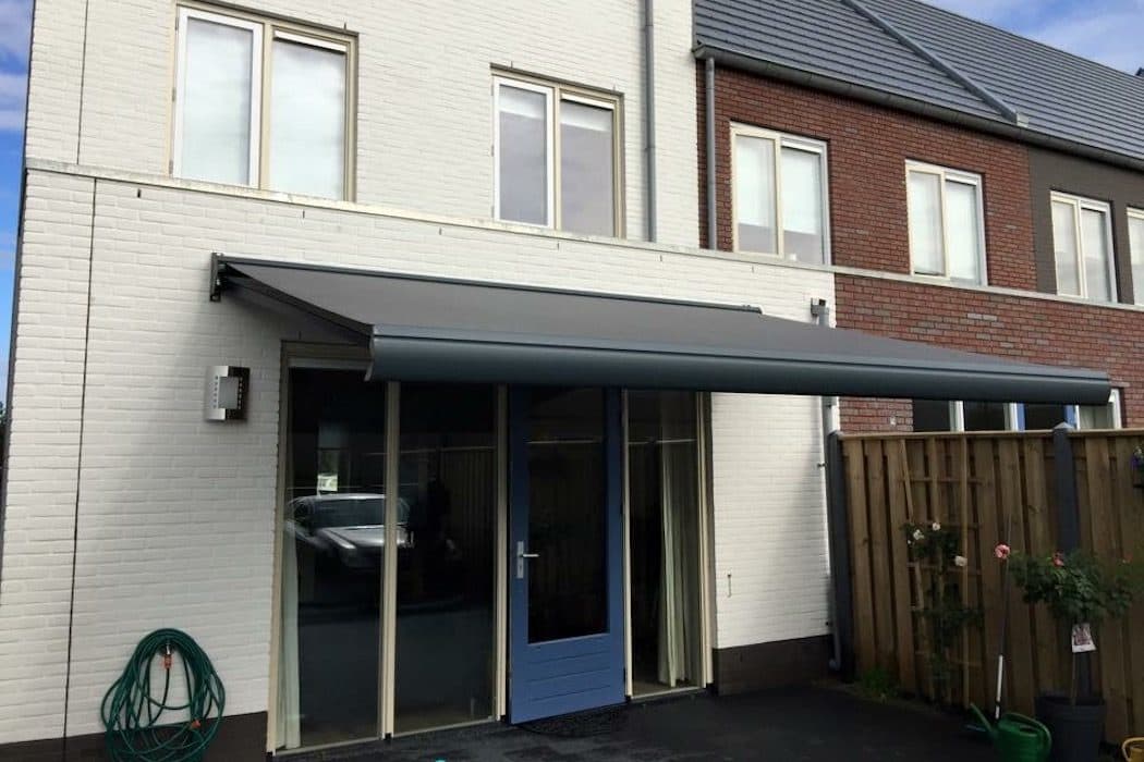 Antraciet knikarmscherm uitgerold boven de achterdeur van een rijwoning