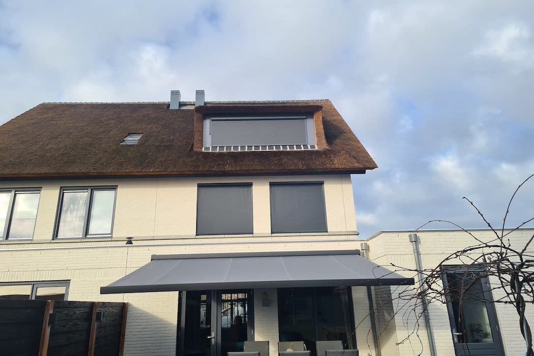 Achtergevel met een antraciet knikarmscherm boven het terras en screens voor de ramen en de dakkapel