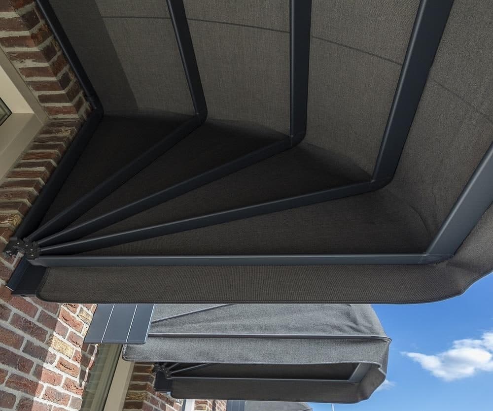 Onderaanzicht van een antraciet aluminium markies met grijs doek tegen een bakstenen gevel
