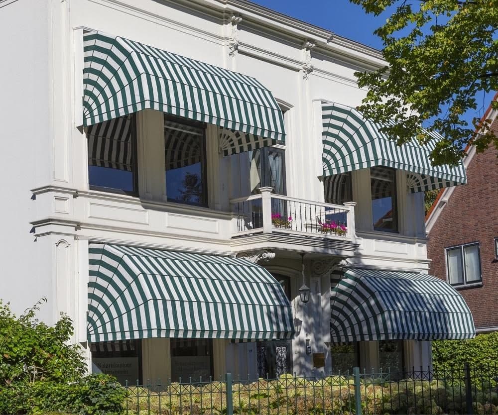 Wit herenhuis met groen-wit gestreepte houten markiezen boven de ramen op de begane grond en de verdieping