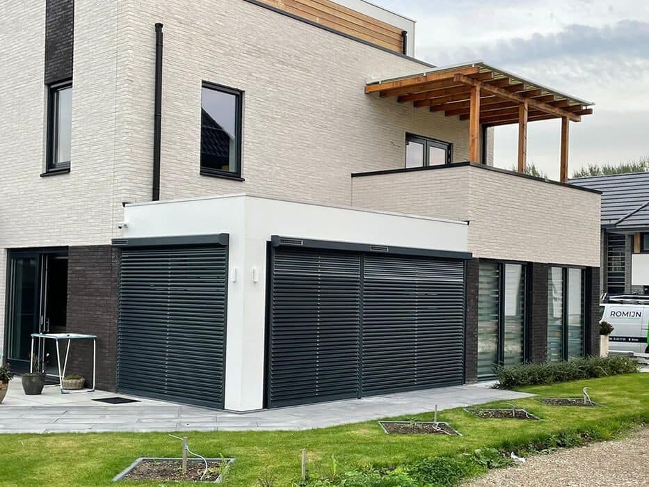 Antraciet rolluiken voor de grote ramen van een moderne woning met witte gevel