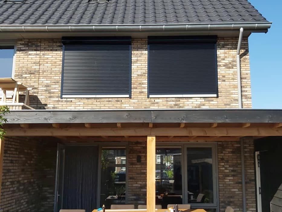 Twee antraciet rolluiken op de verdieping van een woning met houten overkapping op de begane grond