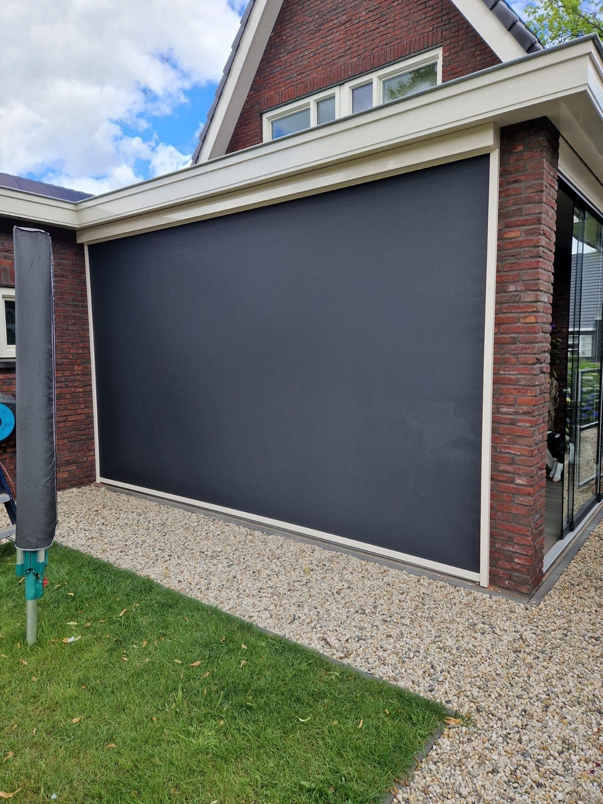 Groot antraciet screen in de zijkant van een overkapping aan een bakstenen woning