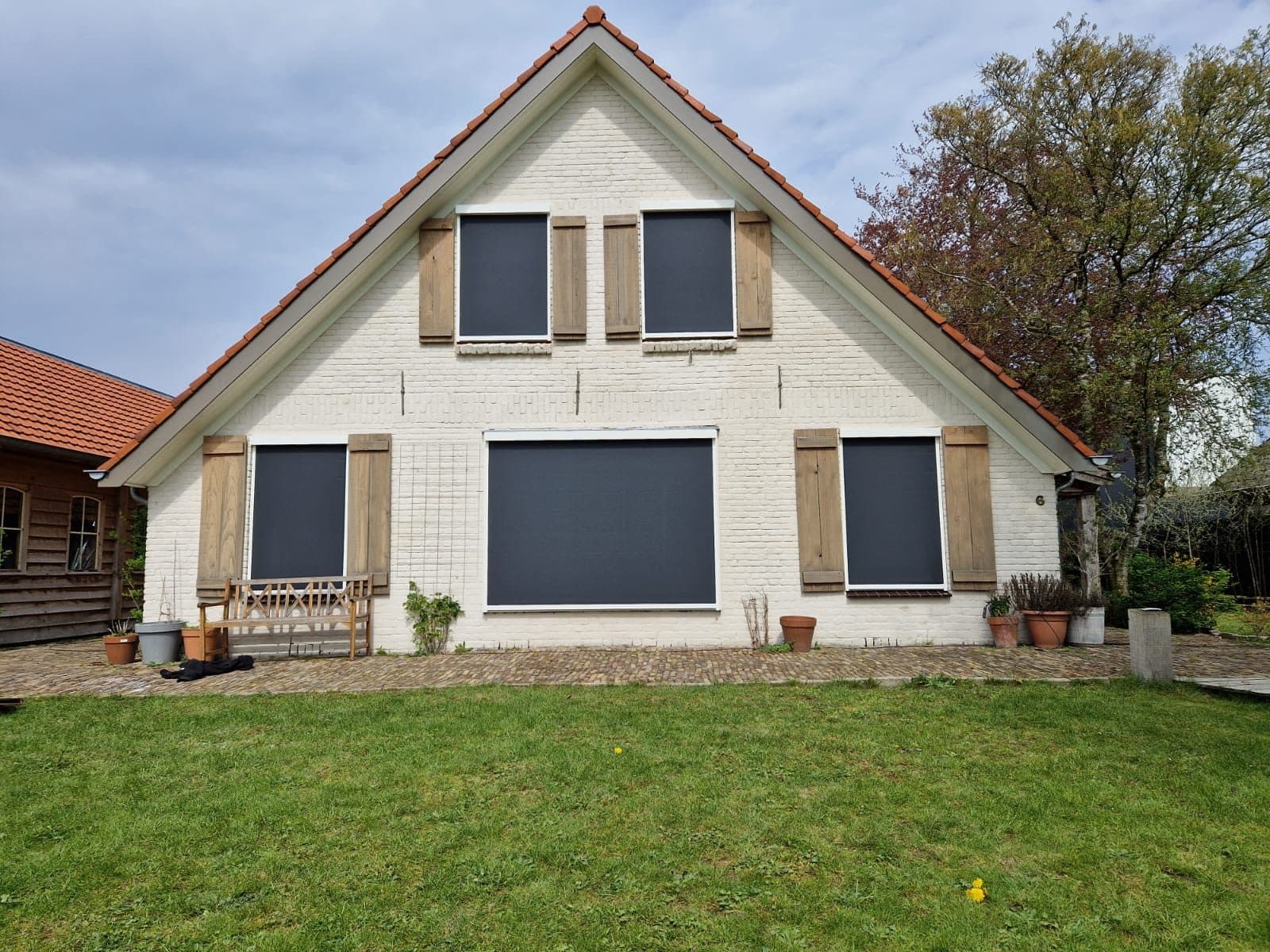 Antraciet screens tussen houten luiken op de witte gevel van een woning met puntdak