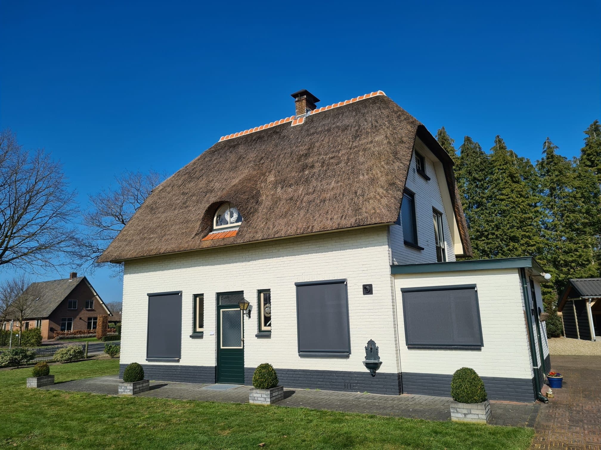 Antraciet screens voor de ramen van een witte woning met rieten dak