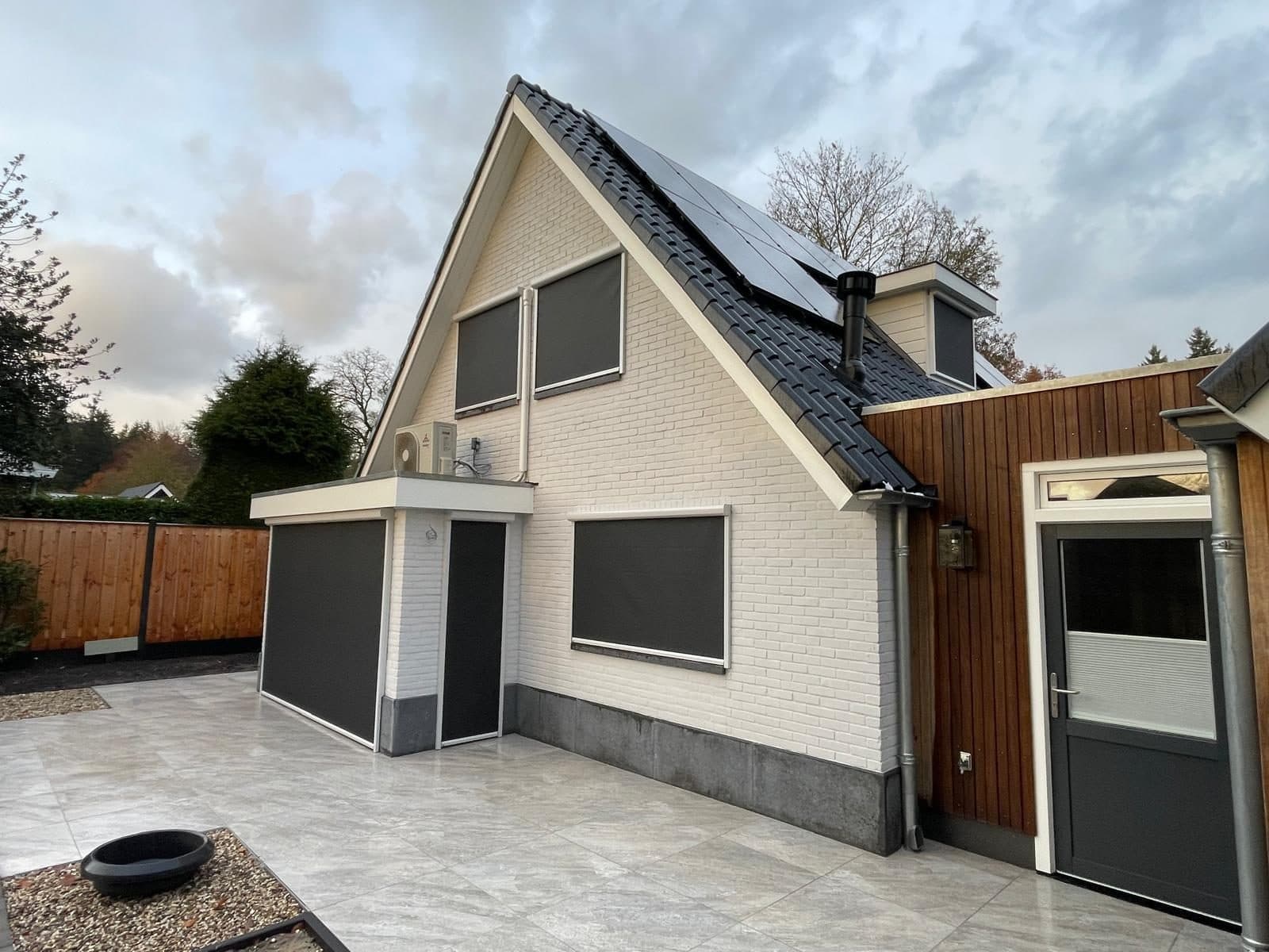 Antraciet screens voor de ramen en de pui van een witte woning, met een licht tegelterras