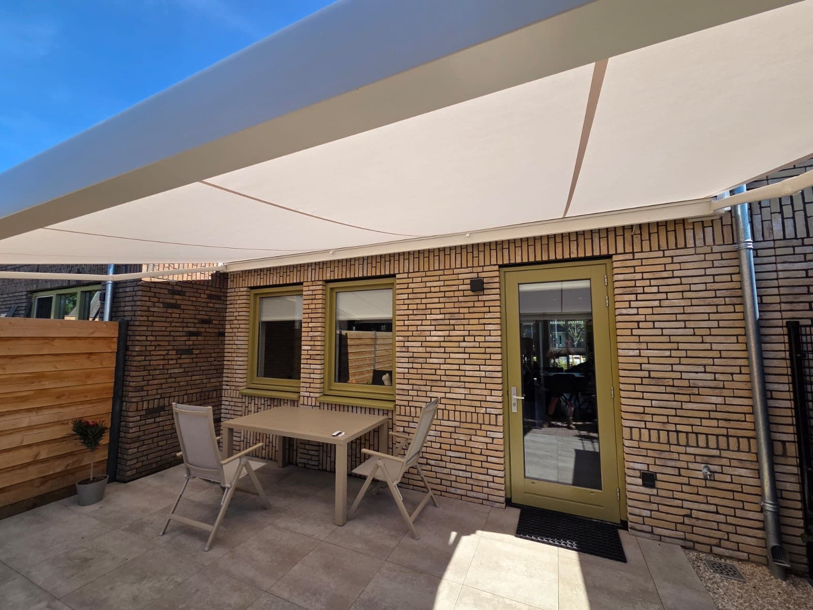 Uitgerold terrasscherm met crèmekleurig doek boven een terras met tuinset, van onderen gezien