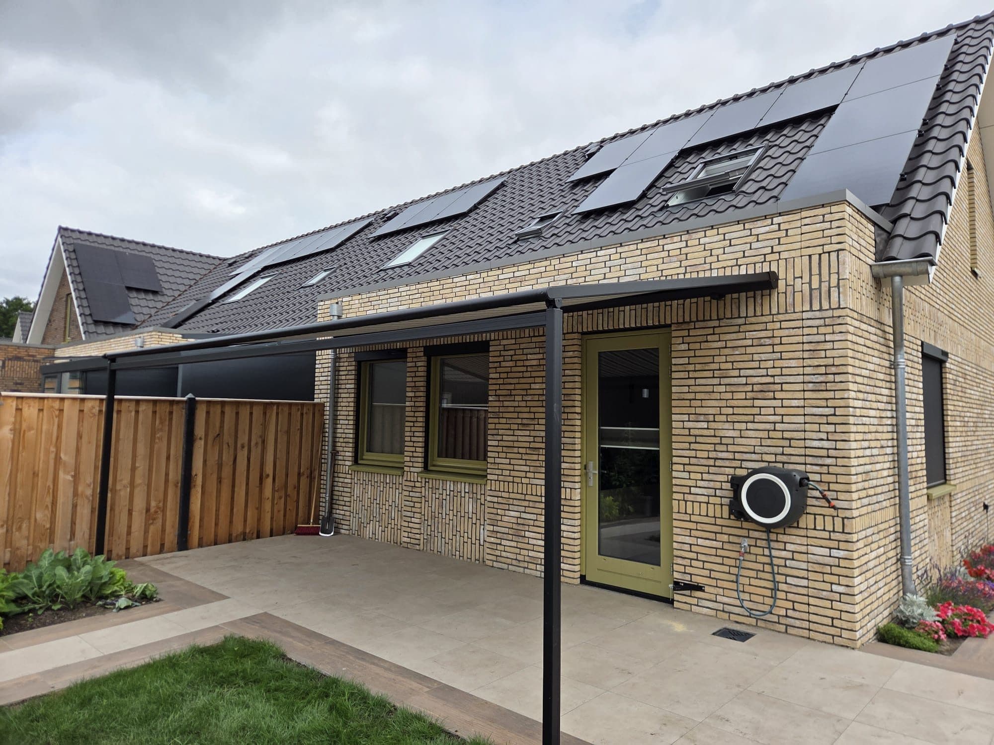 Antraciet zonwering op staanders boven het terras van een nieuwe woning met lichte baksteen