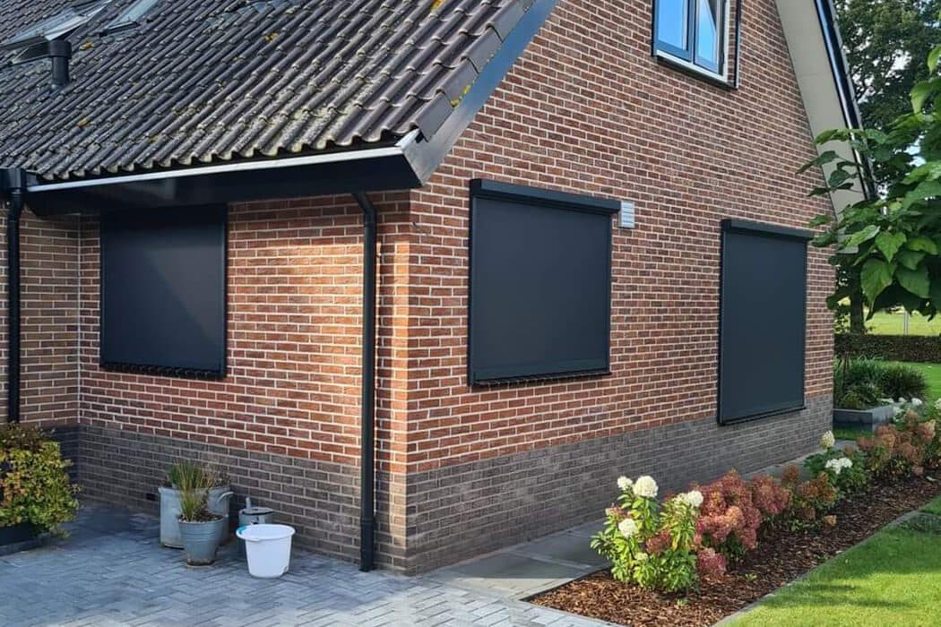 Antraciet screens voor de ramen van een roodbakstenen woning met een border ervoor