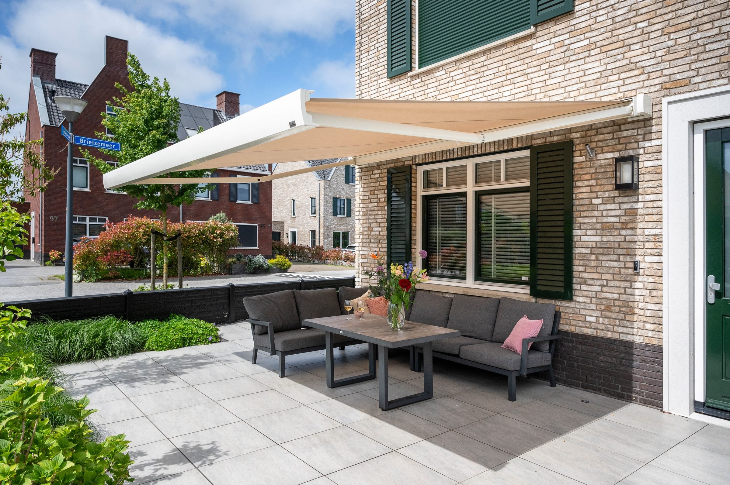 Uitgerold creme knikarmscherm boven een terras met loungeset bij een hoekwoning