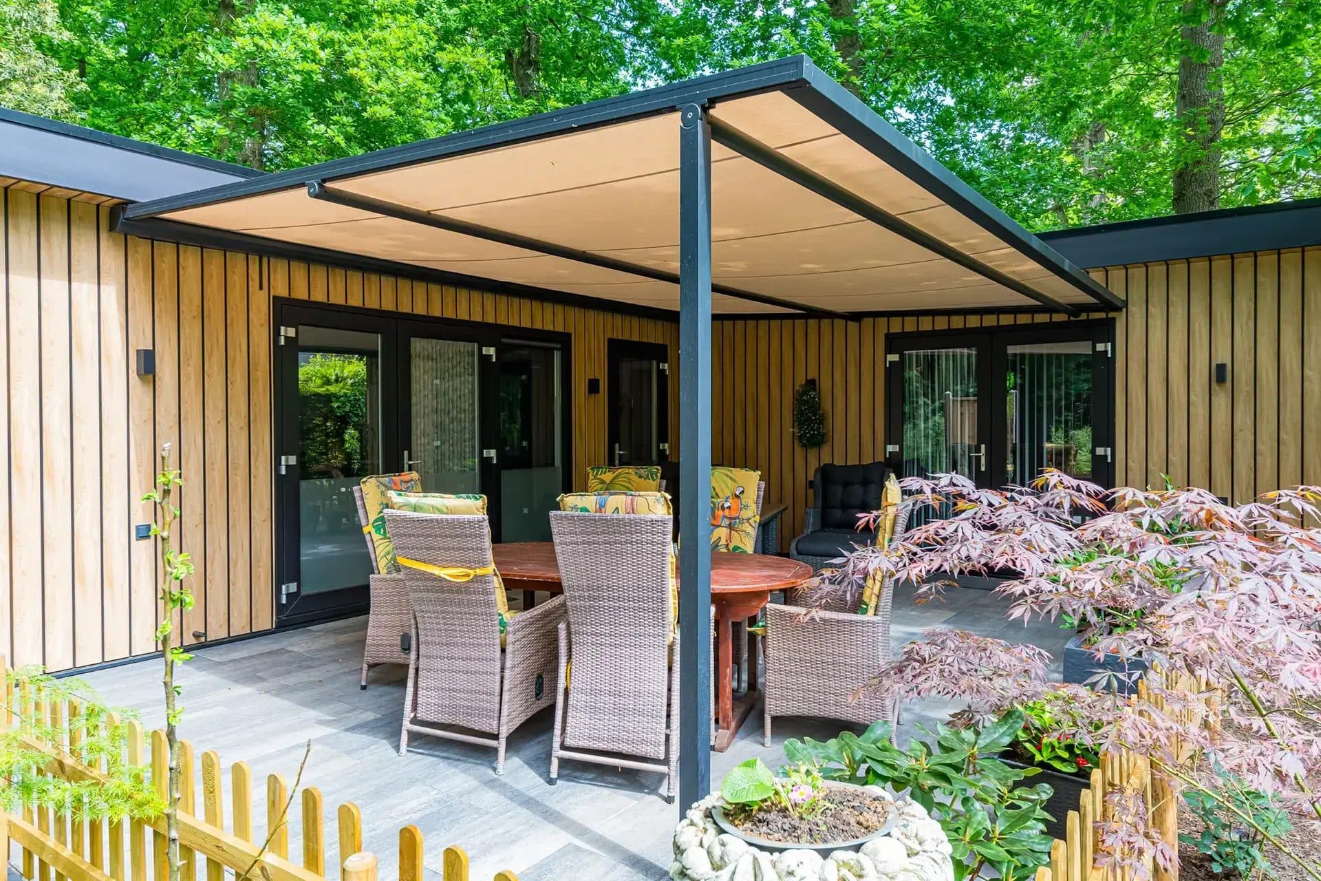 Antraciet pergola met beige doek boven een terras met rieten stoelen en een Japanse esdoorn