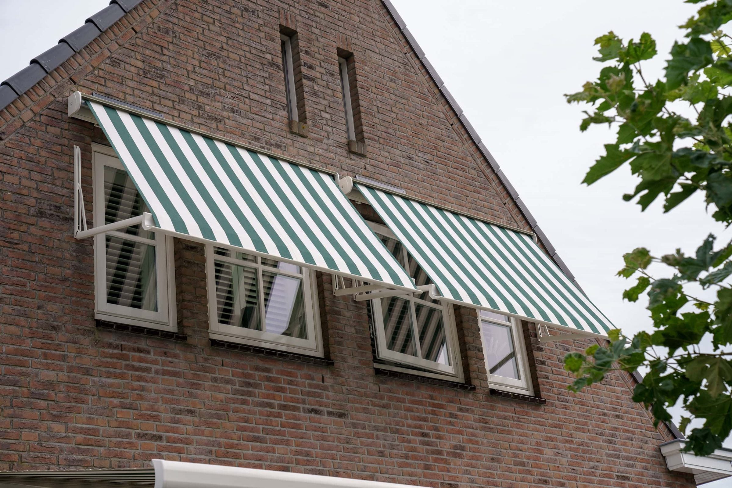 Groen-wit gestreepte uitvalschermen boven de ramen van een bakstenen woning